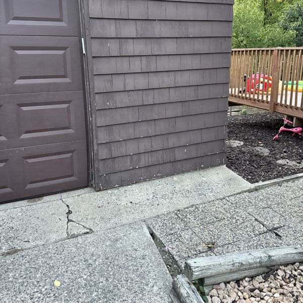 Brown wooden shed with a concrete pathway, leading to a wooden deck with colorful play equipment.