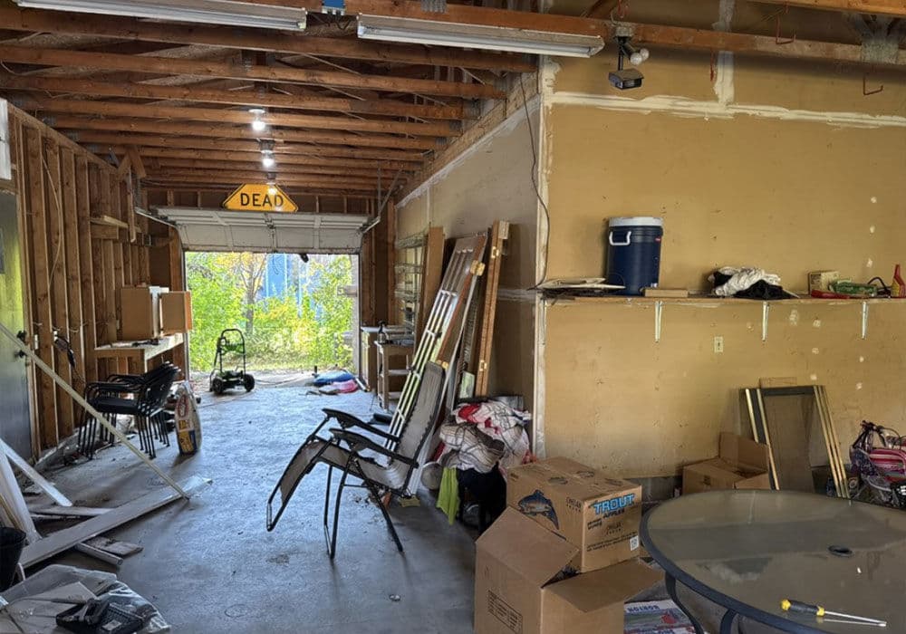 Cluttered garage interior with tools, boxes, and a view of the outdoors through the open door.